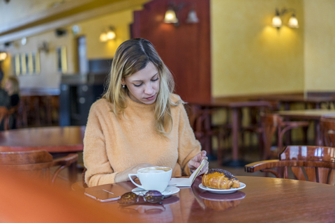 Junge Frau in einem Café mit Notizbuch, Gebäck und Kaffee, lizenzfreies Stockfoto