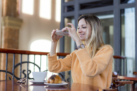 Smiling young woman in a cafe taking cell phone picture stock photo