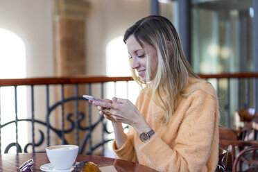 Lächelnde junge Frau in einem Café mit Mobiltelefon - AFVF00247