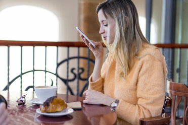 Lächelnde junge Frau in einem Café mit Mobiltelefon - AFVF00248