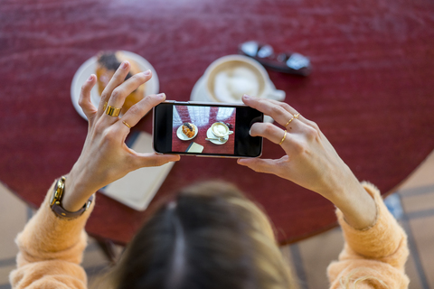 Draufsicht auf eine Frau in einem Café, die ein Handyfoto macht, lizenzfreies Stockfoto