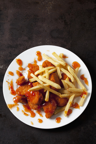 Teller mit Chicken Nuggets mit süßer Chilisauce und Pommes frites auf dunklem Metall, lizenzfreies Stockfoto