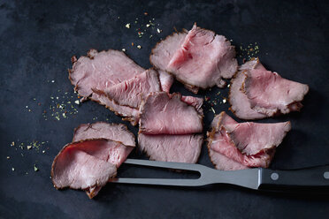 Six slices of roast beef, herbes and meat fork on dark ground - CSF28944