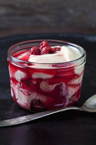 Glass of vanilla custard with raspberries on dark ground stock photo