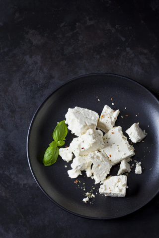 Feta, Kräuter und Basilikumblätter auf schwarzem Teller, lizenzfreies Stockfoto