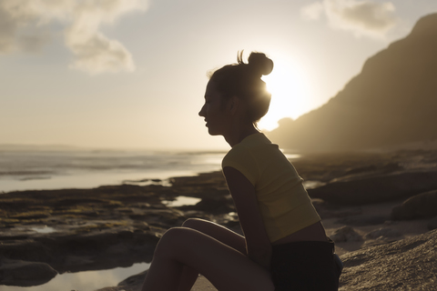 Indonesia, Bali, young woman sitting on the beach at sunset stock photo