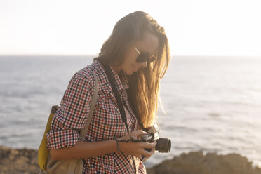 Indonesia, Bali, Lembongan island, young woman with camera at ocean coastline - KNTF01004