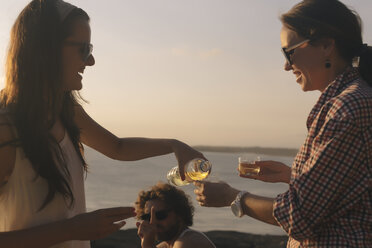 Indonesien, Bali, Insel Lembongan, Freunde bei einem Drink an der Meeresküste in der Abenddämmerung - KNTF01006