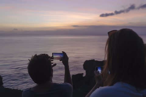 Indonesia, Bali, Lembongan island, friends at ocean coast at dusk taking cell phone pictures stock photo