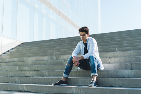 Ernster junger Mann sitzt auf einer Treppe im Freien, lizenzfreies Stockfoto