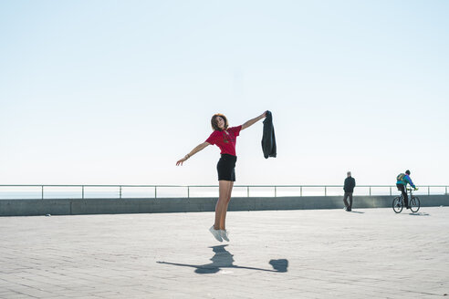 Modische junge Frau, die auf der Uferpromenade springt - AFVF00268