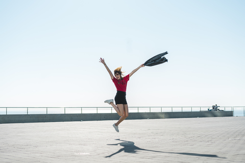 Fashionable young woman jumping on waterfront promenade stock photo