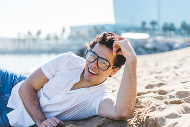 Portrait of happy young man lying in sand on the beach - AFVF00273