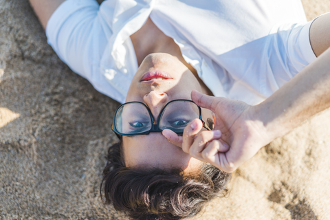 Porträt eines jungen Mannes mit Brille, der im Sand am Strand liegt, lizenzfreies Stockfoto