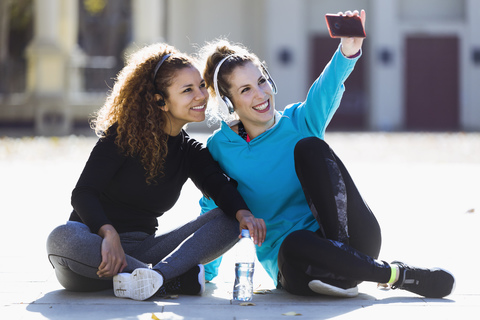 Zwei lächelnde, sportliche junge Frauen, die eine Pause machen und ein Selfie machen, lizenzfreies Stockfoto