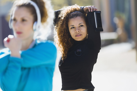 Two focused sportive young women stretching listening to music stock photo