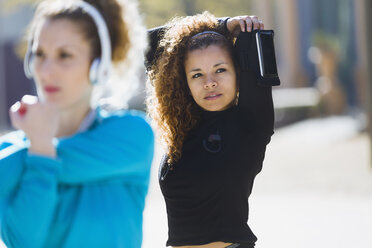 Two focused sportive young women stretching listening to music - JSRF00008