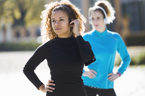 Zwei konzentrierte, sportliche junge Frauen stehen und hören Musik, lizenzfreies Stockfoto