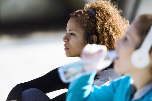 Zwei sportliche junge Frauen, die eine Pause machen und Musik hören - JSRF00015