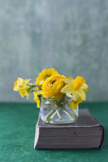 Persischer Hahnenfuß, Narzisse, Schlüsselblume und Hornveilchen in Glas auf einem Buch - MYF02013