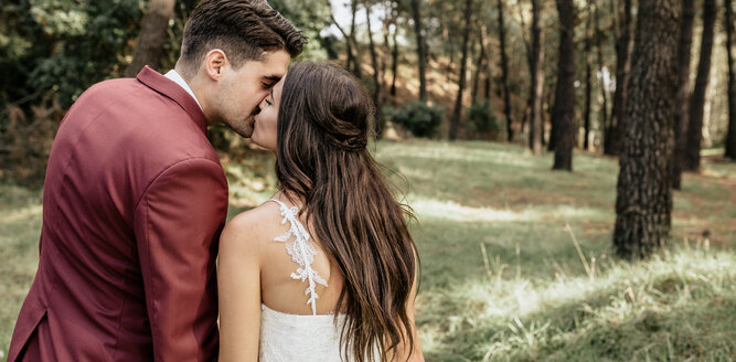 Rückansicht von Braut und Bräutigam, die sich im Wald küssen - DAPF00895