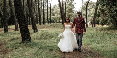 Happy bride and groom walking in forest - DAPF00896