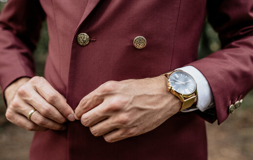 Close-up of man wearing a suit and golden watch buttoning his jacket - DAPF00907