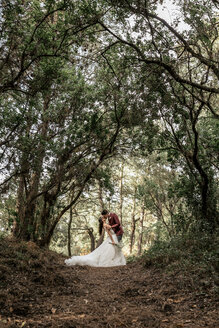 Braut und Bräutigam küssen sich leidenschaftlich unter großen Bäumen im Wald - DAPF00910