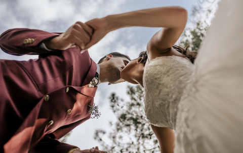 Bride and groom holding hands and kissing with sky in the background stock photo