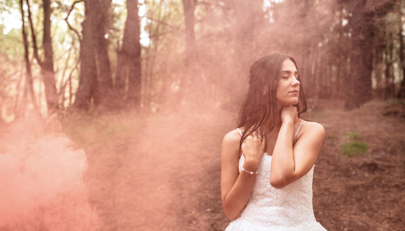 Frau mit geschlossenen Augen im Hochzeitskleid im Wald, umgeben von Rauchwolken - DAPF00919