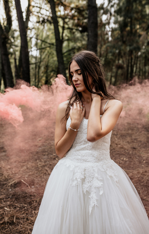 Woman with closed eyes wearing wedding dress in forest surrounded by clouds of smoke stock photo