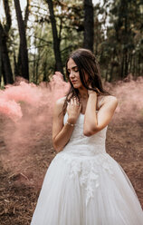 Frau mit geschlossenen Augen im Hochzeitskleid im Wald, umgeben von Rauchwolken - DAPF00920