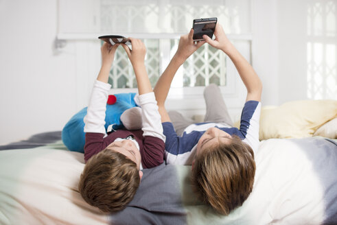 Zwei Jungen liegen zu Hause auf dem Bett und benutzen Handys - SKCF00332