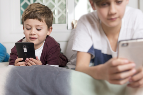 Zwei Jungen liegen zu Hause auf dem Bett und benutzen Handys, lizenzfreies Stockfoto