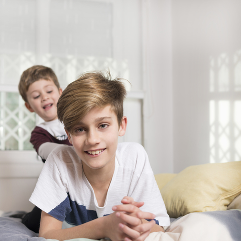 Portrait of smiling boy with younger brother lying on bed at home stock photo