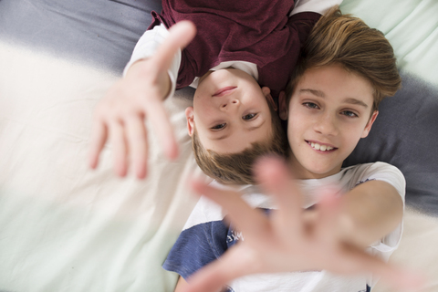 Top view of two smiling brothers lying on bed reaching out their hands stock photo