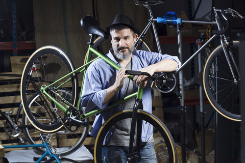 Portrait of confident man in workshop carrying bicycle stock photo