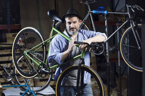 Porträt eines selbstbewussten Mannes in einer Werkstatt mit Fahrrad - JSRF00038