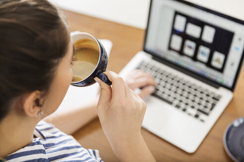 Junge Frau macht eine Kaffeepause bei der Arbeit mit dem Laptop zu Hause - JHAF00017
