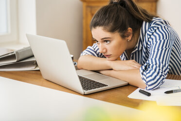 Junge Frau schaut auf den Laptop auf dem Schreibtisch zu Hause - JHAF00019