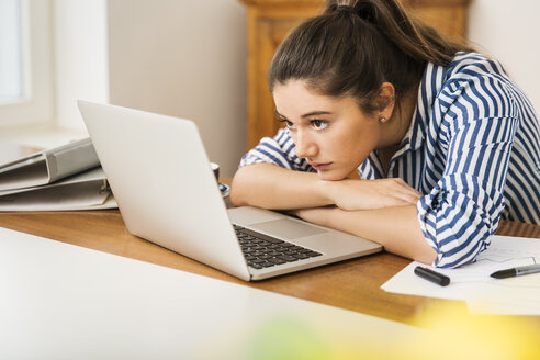 Junge Frau schaut auf den Laptop auf dem Schreibtisch zu Hause - JHAF00019