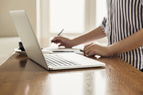 Nahaufnahme einer Frau mit Laptop und Dokumenten auf einem Tisch zu Hause, lizenzfreies Stockfoto