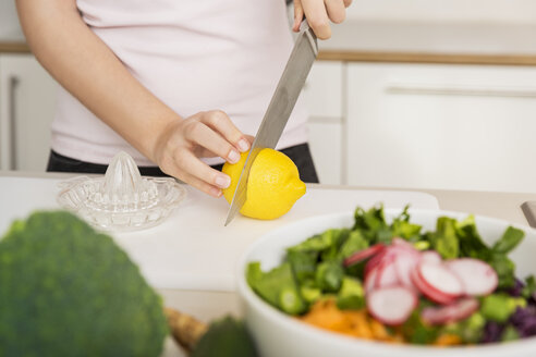 Junge Frau schneidet eine Zitrone für ein frisches Salatdressing - JHAF00024