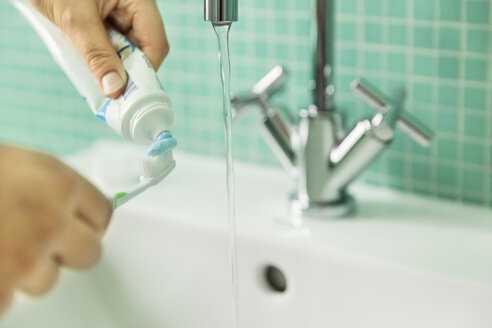 Hands putting toothpaste on toothbrush in bathroom - JHAF00030