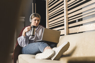 Young woman on couch with coffee and laptop - UUF12825