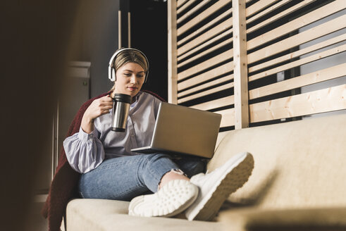 Junge Frau auf Couch mit Kaffee und Laptop - UUF12825