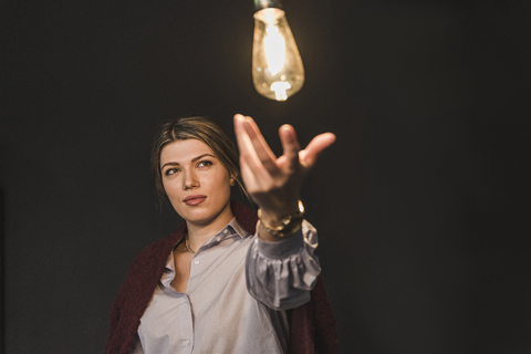 Junge Frau greift nach einer leuchtenden Glühbirne, lizenzfreies Stockfoto