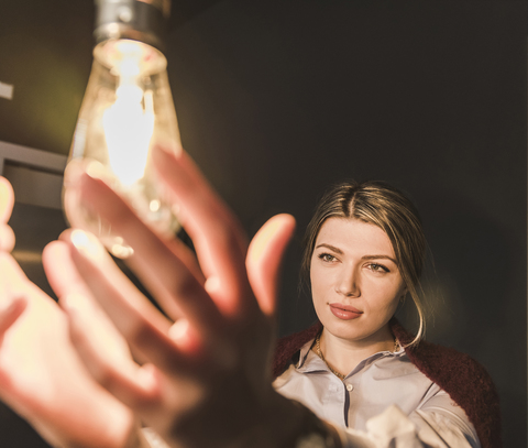 Young woman reaching for illuminated light bulb stock photo
