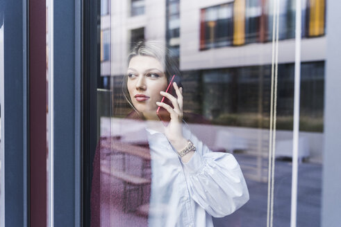 Junge Frau am Handy hinter einer Fensterscheibe - UUF12840