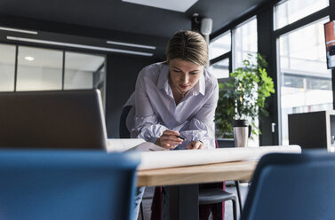 Junge Frau arbeitet an einem Plan am Tisch im Büro - UUF12841